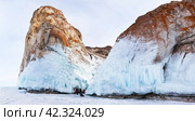 Baikal Lake in winter. Panoramic view of icy Cape Sagan-Khushun or Three Brothers cliffs. Tourists take pictures of beautiful icicles and ice crusts on rocks. Winter travel and outdoors. Стоковое фото, фотограф Виктория Катьянова / Фотобанк Лори