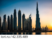 Evening view of silhouettes Dubai city modern skyscrapers at sunset background. Cityscape UAE city with new towers at dusk sky. Construction and modern architecture concept. Copy ad text space, poster. Стоковое AI-изображение, AI-художник Aleksandr Golubev / Фотобанк Лори