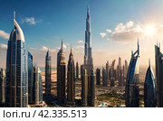 View of modern skyscrapers of Dubai city, UAE with burj khalifa, blue sky background. Amazing urban cityscape of new towers at blue sky. Construction and modern architecture concept. Copy text space. Стоковое AI-изображение, AI-художник Aleksandr Golubev / Фотобанк Лори