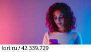 Beautiful young woman using smart phone on bright light pink background. Young igeneration, overuse, modern tech for communication, fun and leisure, AI technologies. Стоковое AI-изображение, AI-художник Alexander Tihonovs / Фотобанк Лори