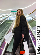 Pretty woman walking up an escalator with shopping bags, turned look at camera. Stylish lady purchase shopping experience in shop mall, enjoy shopping trip. Store lifestyle concept. Copy ad text space. Стоковое фото, фотограф Aleksandr Golubev / Фотобанк Лори