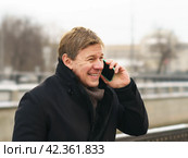 Handsome man walking in the Moscow city center during coronavirus pandemic. New Year holidays. He talking on the smartphone. The conversation is in a positive mood. Moscow cityscape as background. Стоковое фото, фотограф YuryKara / Фотобанк Лори