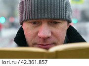 Handsome man in Moscow city center during coronavirus pandemic. New Year holidays. He sitting at the bench and reading the book in the public park. Стоковое фото, фотограф YuryKara / Фотобанк Лори