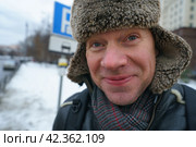 Handsome man walking in Moscow city center. Cold winter in the Russian capital during coronavirus pandemic time. He wear hot cap made of natural sheepskin. It fastened at the chin to protect from cold. Стоковое фото, фотограф YuryKara / Фотобанк Лори