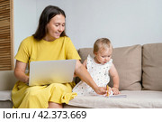 Happy mother taking notes for child while working from home. Multitasking due to maternity leave. Стоковое фото, фотограф Natalia Gdovskaia / Фотобанк Лори