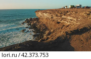 Rocky coastline alongside cliff, blue Atlantic Ocean water reflect at sunset. Nature landscape. Golden sandstone bluff beach. Tourists meet dusk. Travel destination. Fuerteventura Island, Canaries. Стоковое видео, видеограф Igor Tichonow / Фотобанк Лори