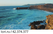 Rocky coastline alongside cliff, blue Atlantic Ocean water reflect at sunset. Nature landscape. Golden sandstone bluff beach. Amazing aerial view. Travel destination. Fuerteventura Island, Canaries. Стоковое видео, видеограф Igor Tichonow / Фотобанк Лори