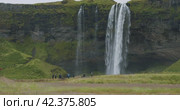 Beautiful Seljalandsfoss waterfall Iceland with unrecognized tourist walking around. Стоковое видео, видеограф Igor Tichonow / Фотобанк Лори