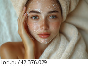 Close up cropped portrait of a young beautiful woman in bath towel smiling applying face body cream on her face for rejuvenation soft moisturizing effect. Spa beauty treatment concept. Body skin care. Стоковое AI-изображение, AI-художник Ирина Михайличенко / Фотобанк Лори
