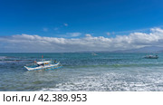 A traditional Filipino boat bangka with a double-outrigger dugout bobs on the waves of the turquoise ocean. On the horizon, against the blue sky and clouds, a mountain range is visible. Philippines (2024 год). Стоковое фото, фотограф Вера Ивановна Кубарева / Фотобанк Лори