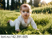 Crying unhappy baby girl crawling in green grass lawn summer urban park, sad depressed. Sorrowful kid creeping in city springtime season. Concept of childhood and baby health care. Copy text space. Стоковое AI-изображение, AI-художник Aleksandr Golubev / Фотобанк Лори