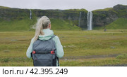 Woman with backpack walks towards the famous Seljalandsfoss waterfall Iceland. Стоковое видео, видеограф Igor Tichonow / Фотобанк Лори