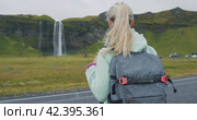 Woman with backpack walks towards the famous Seljalandsfoss waterfall Iceland. Стоковое видео, видеограф Igor Tichonow / Фотобанк Лори