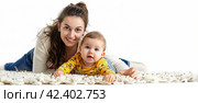 A beautiful young mother and her little son are lying on the floor on a white background and looking at the camera. The concept of maternal happiness. Стоковое AI-изображение, AI-художник Ярославский Максим / Фотобанк Лори