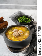 Meatball in a spoon. soup with meatballs in a black bowl and croutons in hard light. A European dish typical of Spain, Sweden, Turkey, and Russia. Meatballs, kyufta, faggots - meat balls in soup. Copy space. Стоковое фото, фотограф Оксана Медведева / Фотобанк Лори