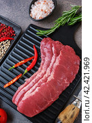 marbled beef bacon. black wooden cutting board with raw marbled beef bacon and seasonings, flat lay on taupe stone background. Стоковое фото, фотограф Оксана Медведева / Фотобанк Лори