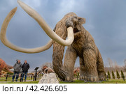 Люди смотрят на фигуру мамонта в Динопарке Янтарного (2024 год). Редакционное фото, фотограф Константин Чижов / Фотобанк Лори