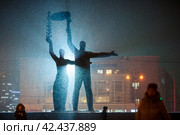 Город Новосибирск, Сибирь, Россия. Красивый советский памятник на площади Ленина. Большие скульптуры мужчины и женщины подсвечиваются контровым светом. Холодный снежный вечер. Сильный снегопад. Достопримечательность Новосибирска. Редакционное фото, фотограф Андрей Степанов / Фотобанк Лори