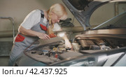 Автосервис. Attractive female mechanic works under bonnet of vehicle in garage workshop. Стоковое видео, видеограф EStarodubov / Фотобанк Лори