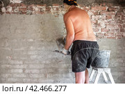 A mature man with a trowel on a stepladder is plastering an old brick wall with a cement-sand mixture. Home repairs. Стоковое фото, фотограф Коханова Наталья / Фотобанк Лори