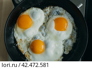 Keto meal eggs frying on hot cast iron frying pan, three fried yellow yolk, ketogenic diet. Стоковое фото, фотограф Natalia Gdovskaia / Фотобанк Лори