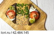 Flat lay with bruschetta spread with cottage cheese and slices of tomato and cucumber on a wooden board with herbs and sunflower seeds. The concept of healthy food. Copy space. Стоковое фото, фотограф Ярославский Максим / Фотобанк Лори