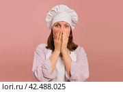 Frightened woman cook on studio pink background. Portrait of a female person in chef's clothing. Стоковое фото, фотограф Андрей Журавлев / Фотобанк Лори