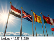 Flags different countries on high flagpoles. National flag different fluttering in wind. Flag Korea, Russia, United States, India, Vietnam, Cambodia and other against blue sky. Natural vertical photo. Стоковое AI-изображение, AI-художник Aleksandr Golubev / Фотобанк Лори