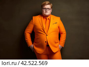Fat chubby blond man with glasses in a orange three-piece suit sits in a armchair on dark studio background, expensively dressed oligarch, tycoon, millionaire. Стоковое AI-изображение, AI-художник Станислав Тарко / Фотобанк Лори