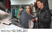Shop assistant helps to choose sweater for the young man in the mall. Стоковое видео, видеограф EStarodubov / Фотобанк Лори