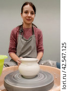 Ceramic pot on potter's wheel in front of woman in apron. Pottery, workshop, ceramics art concept. Modeling of raw fireclay. Стоковое фото, фотограф Константин Григорьев / Фотобанк Лори