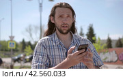 Front view of a walking man with a beard, suddenly bewildered by the news while checking the contents of his smart phone. Стоковое видео, видеограф EStarodubov / Фотобанк Лори