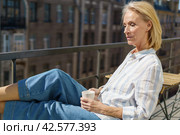 Happy elderly woman sitting on terrace with cup of coffee and enjoying beautiful sunny morning. Стоковое фото, фотограф Natalia Gdovskaia / Фотобанк Лори
