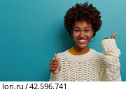 ctp afroamerican young woman in white sweater with thumbs up while pointing to right. Стоковое AI-изображение, AI-художник Юлия Гапеенко / Фотобанк Лори