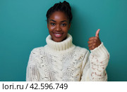 ctp afroamerican young woman in white sweater with thumbs up while pointing to right. Стоковое AI-изображение, AI-художник Юлия Гапеенко / Фотобанк Лори