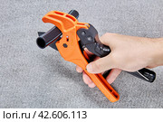 Ratcheting pipe cutter in shape of scissors with polyethylene tube on blade is held in hand of plumber. Стоковое фото, фотограф Владимир Григорьев / Фотобанк Лори