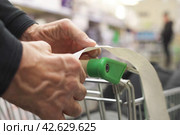 The hands of an unrecognizable older man hold a sales receipt next to a grocery cart in a supermarket. Стоковое фото, фотограф Владимир Федоров / Фотобанк Лори