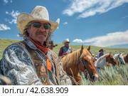 Wild west cowboy riding horse on vast prairie under blue sky with fluffy clouds. Стоковое AI-изображение, AI-художник Юрий Поздников / Фотобанк Лори