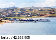 BAIKAL LAKE, OLKHON ISLAND, SAKHYURTA VILLAGE, IRKUTSK REGION, RUSSIA - August 14, 2023: Top view of Sakhyurta village with tourist houses on shore and pleasure ships on pier on summer day. Редакционное фото, фотограф Виктория Катьянова / Фотобанк Лори