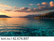 Sunset in laguna of azure Aegean Sea with lush mountains, fluffy clouds, yacht, summer weather. Nature landscape in East Turkey. Concept of vacation, recreation and travel. Стоковое AI-изображение, AI-художник Aleksandr Golubev / Фотобанк Лори