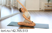 Positive young fit girl in sportswear doing yoga in modern mirrored studio, concentrating on performing revolved easy pose, basic seated posture with crossed legs and twist increasing flexibility. Стоковое видео, видеограф Яков Филимонов / Фотобанк Лори