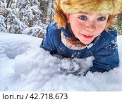 Disabled boy without an arm crawls through the snow while playing snowballs in winter in a snowdrift. The suffering of civilians in the war and confrontation between Ukraine and Russia. Стоковое фото, фотограф Кривошеина Елена Леонидовна / Фотобанк Лори