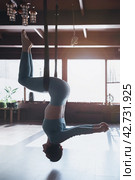 Woman doing aerial yoga, performing Utkatasana exercise, inverted chair pose in a hammock, training alone in sportswear in a yoga studio. Стоковое фото, фотограф Сергей Чайко / Фотобанк Лори