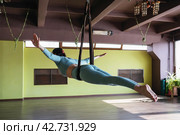 Woman performing balance asana in a hammock, Soaring Sarpasana, snake pose, training alone in sportswear, aerial yoga concept. Стоковое фото, фотограф Сергей Чайко / Фотобанк Лори