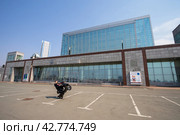 Приморская сцена Государственного академического Мариинского театра, Город Владивосток, Приморский край, Дальний Восток России. По парковке перед зданием театра юноша едет на мопеде на одном колесе. (2023 год). Редакционное фото, фотограф Андрей Степанов / Фотобанк Лори