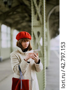 Railway station. Beautiful girl is waiting for train and looks at cell phone. Woman travels light. Стоковое фото, фотограф Natalia Gdovskaia / Фотобанк Лори