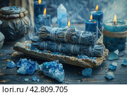 Items that are often associated with meditation, esotericism or relaxation practices. In the center of the frame is a wooden bowl filled with bright blue crystals, likely lapis lazuli stones. To the left of the bowl are bundles of cloth and herbs, similar to resins or smoking sticks, that can be used for space cleansing or aromatherapy. Smoke from the resin floats above the bowl, giving the scene a mystical atmosphere. The background is made up of antique vases and natural wood, which emphasizes the naturalness and traditionality of the scene. Стоковое AI-изображение, AI-художник Анна Кривицкая / Фотобанк Лори