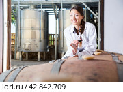 Specialist in white coat examines glass of wine on the background of barrels for fermentation. Стоковое фото, фотограф Татьяна Яцевич / Фотобанк Лори