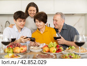 Cheerful family browsing photos on smartphone at home dinner. Стоковое фото, фотограф Яков Филимонов / Фотобанк Лори