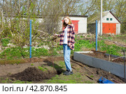 Молодая девушка опустила саженец яблони в лунку и держит его. Стоковое фото, фотограф Роман Лукьянов / Фотобанк Лори